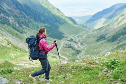 Hiking trip in mountains Romania. Girl with backpack, trekking sticks
