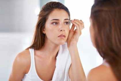 Shaping them to perfection. A young woman tweezing her eyebrows in front of a mirror.